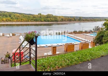 Blauer Pool ohne Menschen am Flussufer im Herbst. Ein großartiger Ort zum Entspannen und Entspannen in der Natur. Der Pool und die Sonnenliegen warten auf Besucher Stockfoto