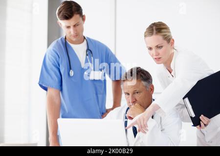 Die beste Behandlung für einen Patienten finden. Drei medizinische Fachkräfte, die zusammen an einem Laptop arbeiten. Stockfoto