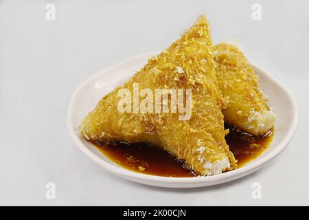 Zwei Stücke Kueh Lopes, eine beliebte Nyonya Peranakan-Leckerbissen aus gekochtem klebriger Reis, serviert mit Kokosraspeln und Palmzucker-Sirup Stockfoto