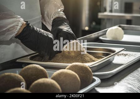 Ein Bauer in schwarzen Handschuhen streut schwarzen Pfeffer auf eine Käsebulle. Der Herstellungsprozess von würzigem Belper knolle Käse Stockfoto