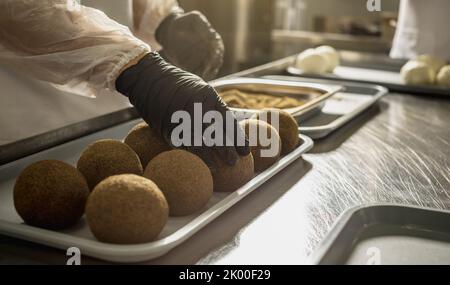 Ein Bauer in schwarzen Handschuhen streut schwarzen Pfeffer auf eine Käsebulle. Der Herstellungsprozess von würzigem Belper knolle Käse Stockfoto