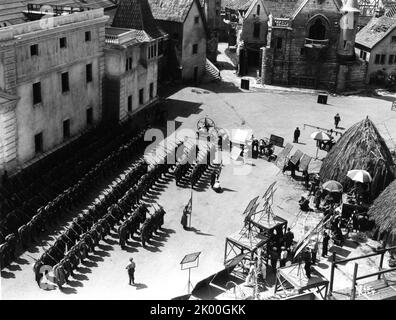 Am Set offene Dreharbeiten Parade deutscher Soldaten auf Universal Studios Lot mit einem Teil von Paris aus Lon Chaneys Glöckner von Notre Dame (1923) oben rechts und Native Huts from the Invisible Ray (1936) (mit Boris Karloff und Bela Lugosi) Behind the Movie / Camera Crew während der Dreharbeiten ZUR ROAD BACK 1937 Regisseur JAMES WHALE Roman Erich Maria Remarque Musik Dimitri Tiomkin Kunstleitung Charles D. Hall Universal Bilder Stockfoto