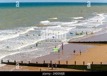 Die Menschen surfimg in brechenden Wellen vom Sandstrand, Cromer, North Norfolk, England, Großbritannien Stockfoto