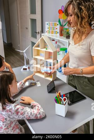 Die Lehrerin erklärt ihren Schülern die Teile eines nachhaltigen Hauses mit einem Elektroauto Stockfoto