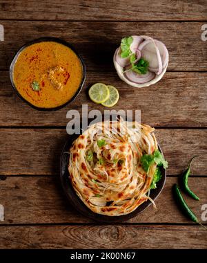 Parotta - ein indisches Brot aus Mehl, das zu schuppiger Knusprigkeit gekocht und mit authentischer südindischer Hühnersalna (kurma) serviert wird Stockfoto