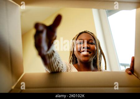 Glückliche afroamerikanische Frau, die in die Box schaut und von niedlichen Haustieren überrascht ist Stockfoto