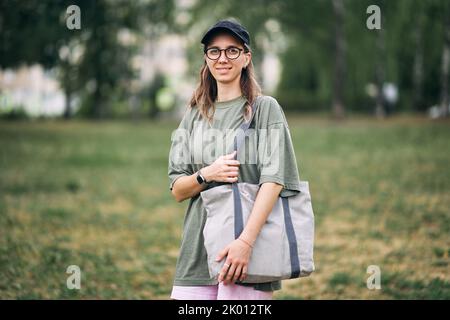 Junge Frau mit Brille mit leerer Öko-Tasche aus Baumwolle, Mockup-Design. Stockfoto