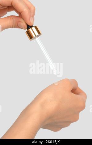 Eine Glaspipette in der Hand einer Frau tropft ätherisches Öl auf ihre Hand. Kosmetische Verfahren Stockfoto