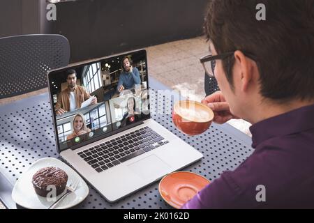 Über der Schulter gesehen, wie ein asiatischer Mann Kaffee trinkt und mit verschiedenen Kollegen einen Videoanruf auf einem Laptop führt Stockfoto