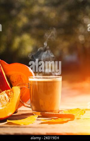 Kürbis Latte Kaffee mit Gewürzen und Zimt. Herbstlicher Heißgetränk auf einem rustikalen Holztisch, der mit gelben Blättern und Kürbis unter der Sonne dekoriert ist. Gemütlichkeit, halloween, Wärme Konzept. . Hochwertige Fotos Stockfoto