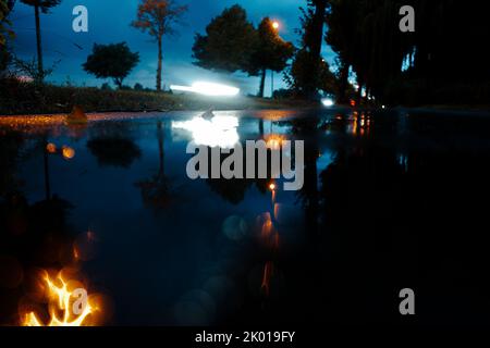 Abstrakter und verschwommener Blick auf die stürmische Nacht am Straßenrand mit vorbeifahrenden Rücklichtern von Autos, die leichte Spuren hinterlassen Stockfoto