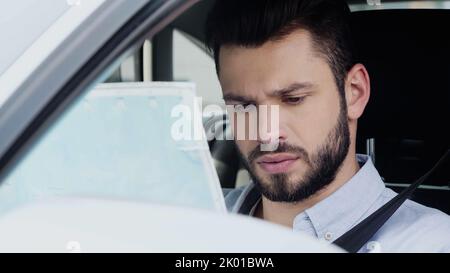 Junger und nachdenklicher Mann, der die Lage einschätzt, während er im Auto sitzt und auf die Karte schaut, Bild aus dem Stock Stockfoto