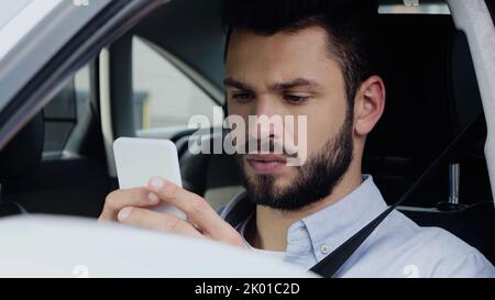 Nachdenklicher Mann, der die Route auf dem Smartphone schätzt, während er im Auto sitzt, Stockbild Stockfoto