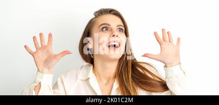 Das Porträt einer jungen kaukasischen Frau im weißen Hemd hebt die Hände und lacht positiv mit offenem Mund, der vor weißem Hintergrund aufschaut Stockfoto