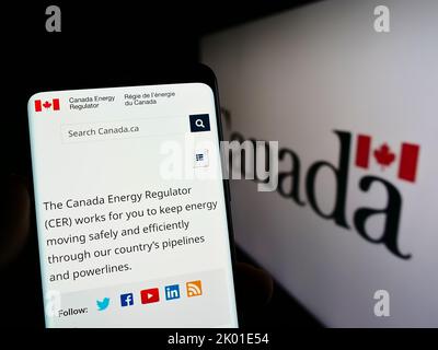 Person mit Smartphone und Website der kanadischen Agentur Canada Energy Regulator (CER) auf dem Bildschirm mit Logo. Konzentrieren Sie sich auf die Mitte des Telefondisplays. Stockfoto