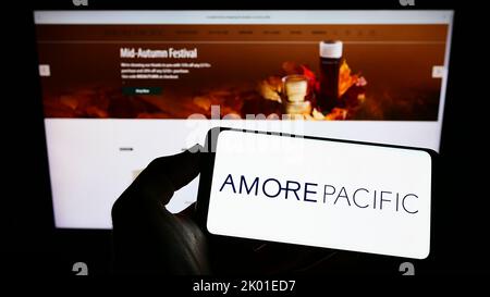 Person, die Mobiltelefon mit Logo der südkoreanischen Firma Amorepacific Corporation auf dem Bildschirm vor der Webseite hält. Konzentrieren Sie sich auf die Telefonanzeige. Stockfoto