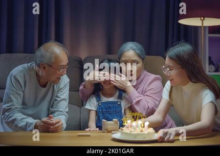 Geburtstagsüberraschung Konzept. Glückliche asiatische Familie Großeltern und Mutter feiern genießen singen Geburtstagslied Party mit Kuchen der Enkelin weht Stockfoto