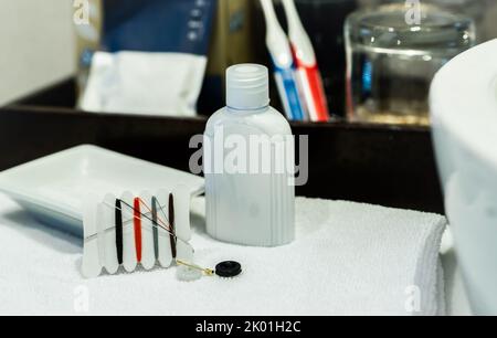 Nähset und Handcreme im Hotelbadezimmer. Kleines tragbares Gewinde-Reparatur-Notfallset mit Nadeln, Knöpfen, Gewinde und Sicherheitsnadeln Stockfoto