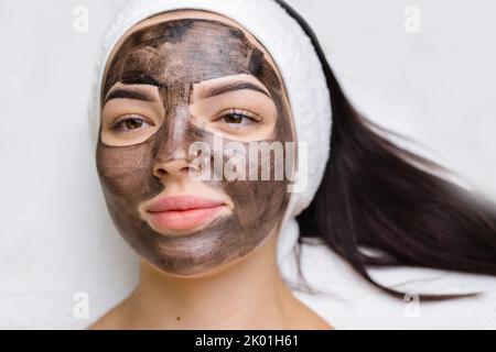 Kosmetologe, der schwarze Maske auf hübsches Frauengesicht mit schwarzen Handschuhen aufträgt, wunderschöne Frau im Spa, die Gesichtsbehandlungen hat Stockfoto