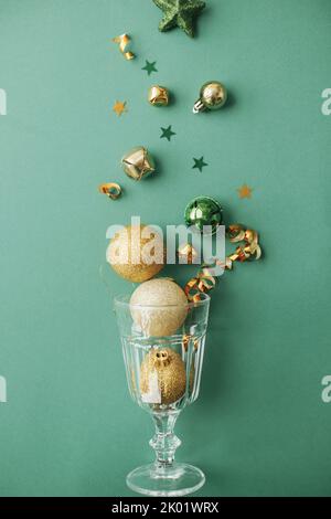 Party-Konzept für das neue Jahr. Stilvolle weihnachten Goldkugeln und Konfetti Gießen aus Champagner-Glas auf grünem Hintergrund flach legen. Frohes neues Jahr und Merr Stockfoto