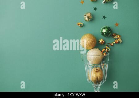 Frohes neues Jahr und frohe Weihnachten! Stilvolle weihnachten Goldkugeln und Konfetti Gießen aus Champagner-Glas auf grünem Hintergrund flach legen. Kreative se Stockfoto