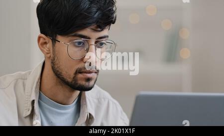 Nahaufnahme männliches Gesicht arabischer hispanischer Mann bärtiger Typ, der mit einem Laptop arbeitet, fühlt sich unter Kopfschmerzen gestresst nimmt die Brille ab und reibt die Augen besorgt um sie Stockfoto