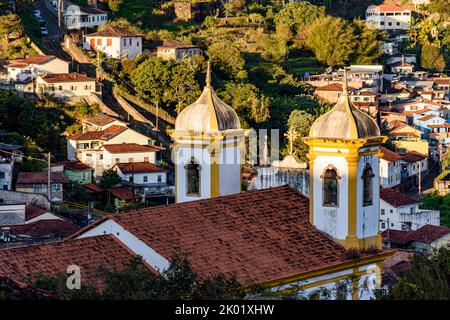 Türme und Glocken einer alten Barockkirche mit den Häusern der Stadt Ouro Preto im Hintergrund Stockfoto