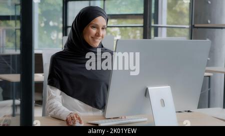 Glückliche erfolgreiche arabische Geschäftsfrau in Hijab Eingabe auf der Tastatur arbeiten am Computer genießen Arbeit online im modernen Büro lächelnde weibliche Manager Stockfoto