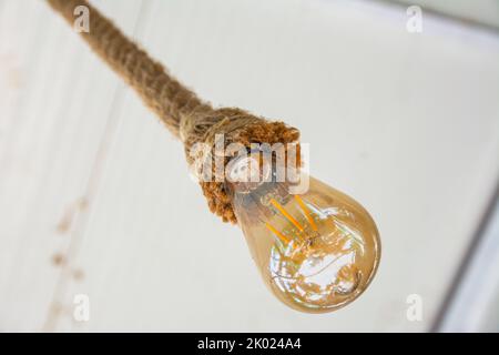 Eine alte Glühbirne hängt an einem Seil von der Decke. Eine wunderschöne dekorative Glühbirne wird aus nächster Nähe aufgenommen. Stockfoto