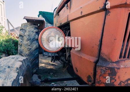 Alte rote Oldtimer-Traktor mit offenem Fahrerhaus. Foto eines ländlichen Traktors ohne Fahrerhaus. Nahaufnahme der Vorderseite des Traktors: Kühler, Scheinwerfer. Stockfoto