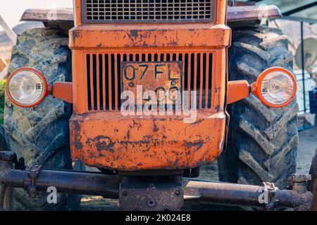 Alte rote Oldtimer-Traktor mit offenem Fahrerhaus. Foto eines ländlichen Traktors ohne Fahrerhaus. Nahaufnahme der Vorderseite des Traktors: Kühler, Scheinwerfer. Stockfoto