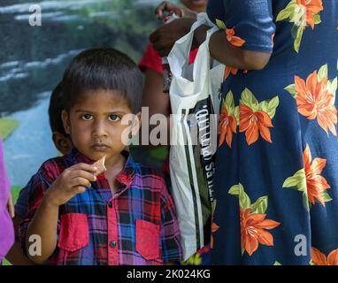 Armes Kind, das in Sri Lanka eine Schokolade isst, während es seine Mutter hält 30.. Juli 2022 Stockfoto