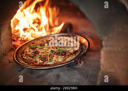 Frische Pizza im Ofen mit Feuer und Holz Stockfoto