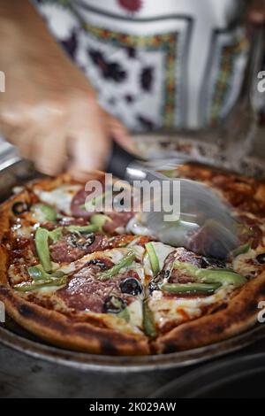 Closeup Hand Koch Bäcker schneiden Pizza in Küche Stockfoto