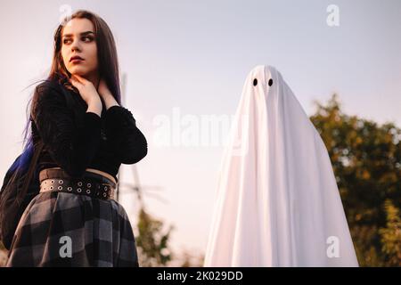 Junge Frau schaut weg, während sie an Halloween mit Geist im Freien steht Stockfoto