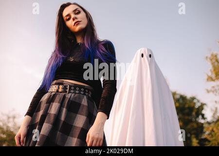 Junge Frau, die an Halloween mit Gespenst gegen den blauen Himmel steht Stockfoto