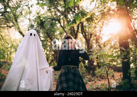 Teenager-Mädchen, das an Halloween mit Geist im Wald an der Hand läuft Stockfoto