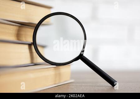 Lesen, Bildung und Forschung Konzept - Stapel von Büchern und Lupe auf dem Tisch in der Bibliothek Stockfoto