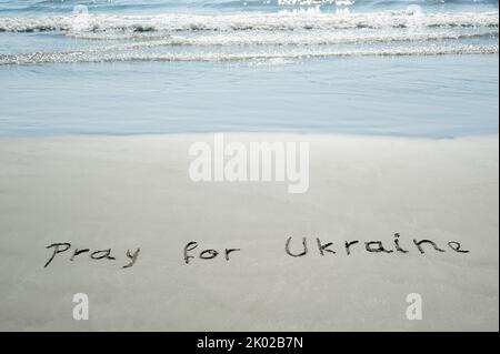 Konzept oder Konzept Gebet für die Ukraine handgeschriebener Text im Sand an einem Strand mit Wellen auf einer exotischen Insel für Religion, Hoffnung, Frieden, Hilfe, Unterstützung, com Stockfoto
