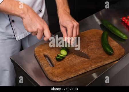 Beschnittene Ansicht des Küchenchefs beim Schneiden von Gurken auf einem Holzschneidebrett, Stockbild Stockfoto
