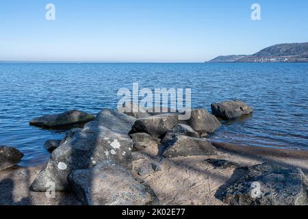 Felsbrocken als Teil eines Wellenbrechers in einem See. Bild vom See Vattern, Schweden. Blaues Wasser und Himmel im Hintergrund Stockfoto