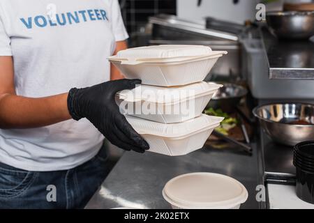 Beschnittene Ansicht eines jungen afroamerikanischen Sozialarbeiters, der Kunststoffbehälter in der Küche hält, Bild aus dem Bestand Stockfoto