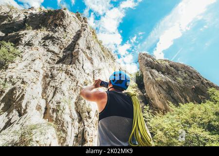 Kletterer Mann in Schutzhelm mit Kletterseil auf der Schulter machen die Klippe Foto mit modernen Smartphone in Paklenica zwischen Felsen Klippe wal Stockfoto