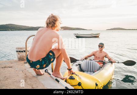 Vater mit Teenager-Sohn auf dem leuchtend gelben aufblasbaren Kajak, der von der Abendfahrt am Adriatischen Hafen in Kroatien in der Nähe von Sibeni zurückkehrt Stockfoto