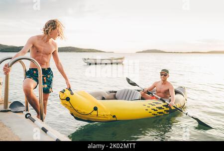 Vater mit Teenager-Sohn auf dem leuchtend gelben aufblasbaren Kajak, der von der Abendfahrt am Adriatischen Hafen in Kroatien in der Nähe von Sibeni zurückkehrt Stockfoto