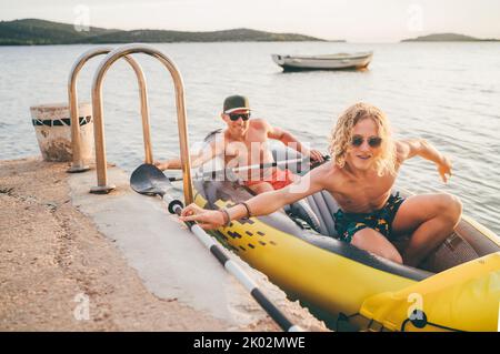 Vater mit Teenager-Sohn auf dem leuchtend gelben aufblasbaren Kajak, der von der Abendfahrt am Adriatischen Hafen in Kroatien in der Nähe von Sibeni zurückkehrt Stockfoto