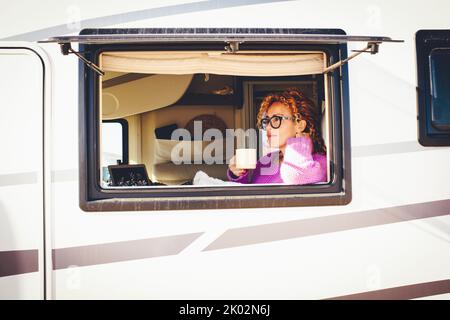 Außenansicht der hübschen Reisenden Dame mit Freizeit entspannen in ihrem Wohnmobil aus dem Fenster gesehen. Fahrzeug reanting Urlaub Urlaub und van Leben Lifestyle Menschen. Heitere weibliche Menschen in rv Stockfoto