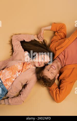 Draufsicht auf fröhlichen und jungen Rotschopf Mann liegend zusammen mit hübschen Freundin auf beige, Stockbild Stockfoto