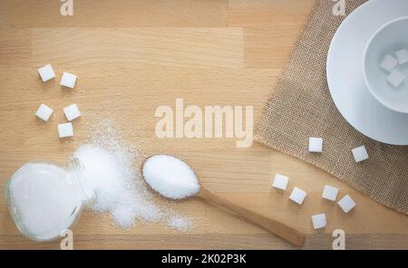 Weißer Zucker und Zuckerwürfel in Holzlöffel auf Holzhintergrund mit Kopierraum, Kaffeebecher mit Zuckerwürfeln Stockfoto