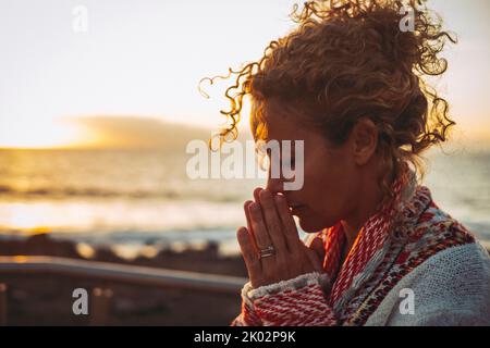 Meditation und innere Balance inneres Glückskonzept mit Seitenportrait einer jungen Frau, die im Freien betet und meditiert, mit Sonnenuntergang im Ozean im Hintergrund. Konzept der psychischen Gesundheit Lebensstil Stockfoto